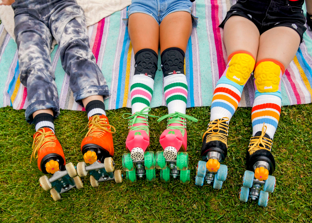 Three skaters sitting on a blanket photographed from the waist down. They are all wearing customized roller skates fitted to their skate styles.